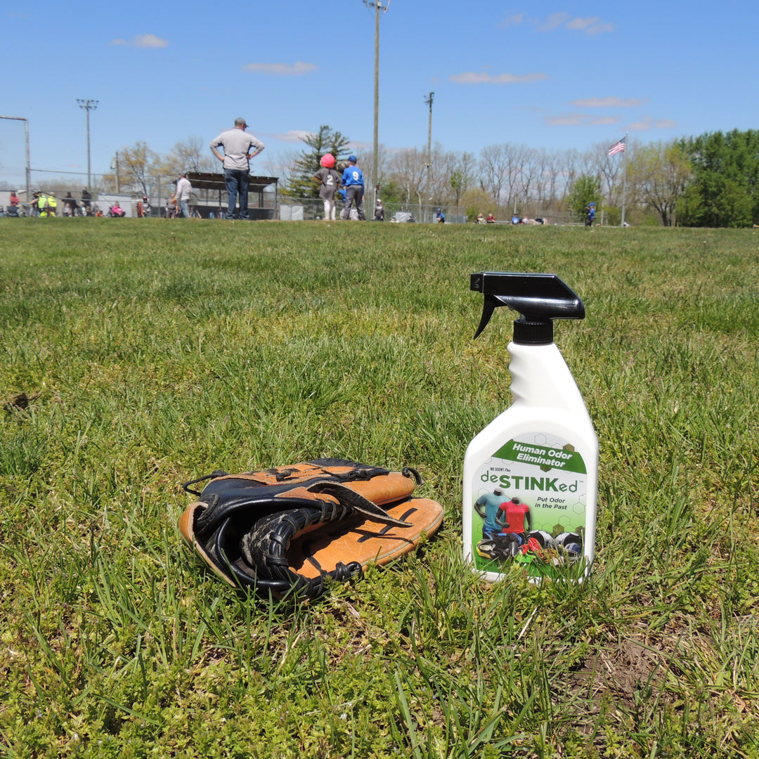 deSTINKed Human Odor Eliminator sits next to a baseball glove in the outfield while kids play.